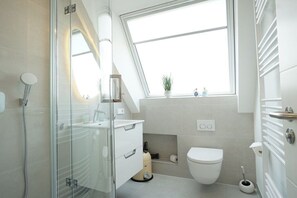 A modern bathroom with a skylight, a glass shower enclosure, a toilet, and a small sink area. - Holiday apartment in Hörnum with Wi-Fi (Hörnum)