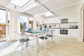 A modern kitchen with a glass dining table, clear chairs, and white cabinetry. - Holiday apartment in Hörnum with Wi-Fi (Hörnum)
