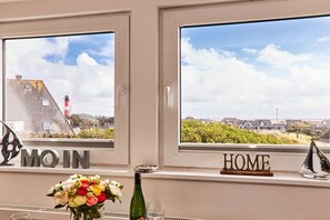 A room with two windows, one labeled 'MO IN' and the other 'HOME', with a view of a lighthouse and houses. - Holiday apartment in Hörnum with parking (Hörnum)