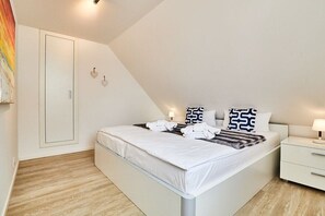 A modern bedroom with a bed, bedside tables, and a wardrobe. - Holiday apartment in Hörnum with parking (Hörnum)