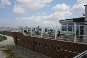 A coastal building with a terrace overlooking the beach, featuring outdoor seating and a view of the sea. - Paradise on the dike, House B (Neßmersiel)