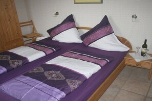A double bed with a purple and white bedspread, two pillows, a wooden nightstand with a wine bottle and glasses, and a wooden wardrobe. - Paradise on the dike, House B (Neßmersiel)