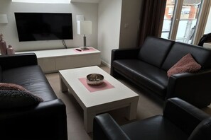 A modern living room with a flat-screen TV, a white coffee table, a black sofa, and a black leather couch. - Holiday apartment with 3 bedrooms (Norderney)