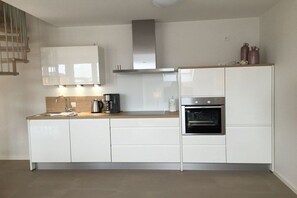 A modern kitchen with white cabinetry, a stainless steel range hood, a built-in oven, and a wooden countertop. - Holiday apartment with 3 bedrooms (Norderney)