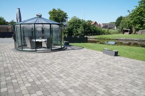 A gazebo with a glass roof and seating area, surrounded by a paved walkway and greenery. - Küsters holiday apartment "Tina" (Hinte)