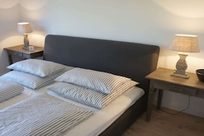 A neatly made bed with striped pillows and a dark headboard, flanked by two bedside tables with lamps. - Holiday apartment in Sylt with 2 bedrooms (Wenningstedt)