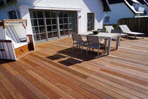 A wooden deck with a table and chairs, a sun lounger, and a windowed patio area. - Holiday apartment in Sylt with 2 bedrooms (Wenningstedt)