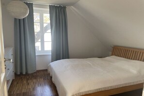 A bedroom with a bed, a window with curtains, a dresser, and a hanging light fixture. - Apartment on the east side (Mönchgut, OT Gager)
