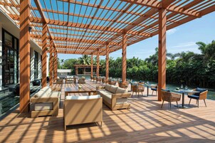 Un área de estar al aire libre con pérgolas de madera, muebles de mimbre y una piscina.