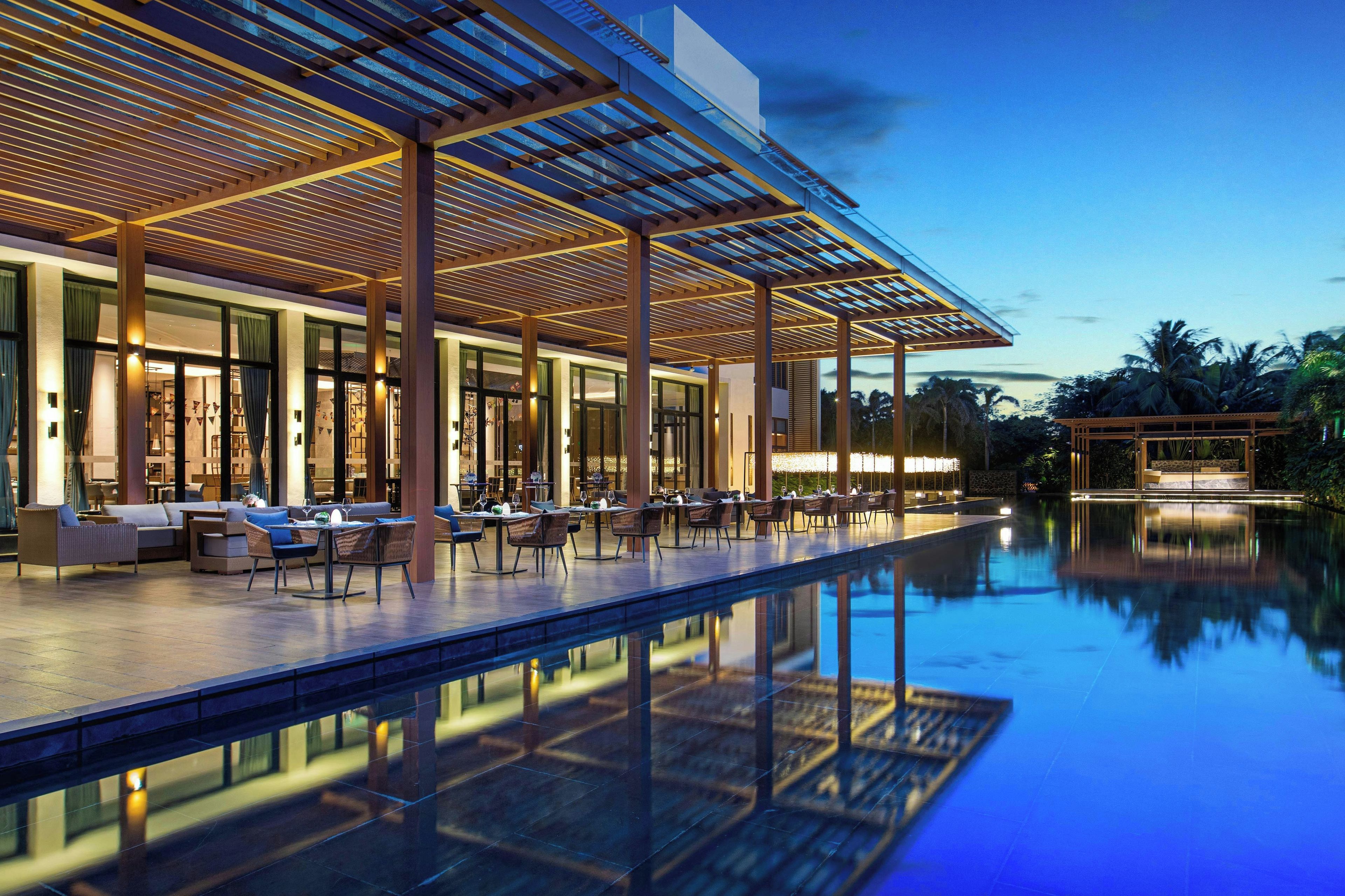 A modern outdoor dining area with a pool, featuring a covered seating area and a clear view of the pool.