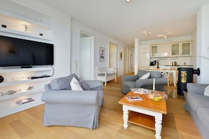 A modern living room with a flat-screen TV, grey sofas, a wooden coffee table, and a kitchen area with cabinets and a kettle. - Holiday apartment with 2 bedrooms (Sassnitz)