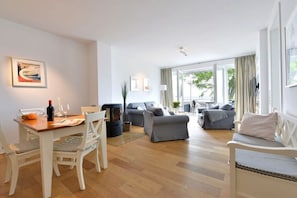 A modern living room with a dining area, a fireplace, and a large window. - Holiday apartment with 2 bedrooms (Sassnitz)