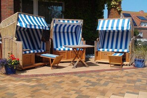 An outdoor seating area with striped awnings, wicker furniture, and a brick floor. - Holiday apartment with 1 bedroom (Norderney)