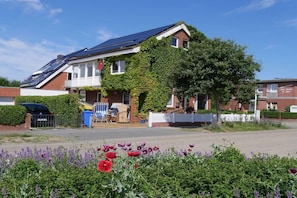 A residential house with solar panels on the roof, a white fence, and a garden with purple flowers. - Holiday apartment with 1 bedroom (Norderney)