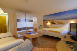 A bedroom with a bed, a desk, a sofa, and a painting on the wall. - Holiday apartment with 1 bedroom (Norderney)