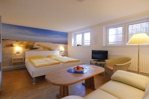 Ein Zimmer mit einem Bett, einem Fernseher, einem Tisch mit Obst und Blick auf den Strand.