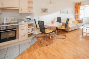A modern kitchen with a dining area, including a round table and chairs, and a sofa with cushions. - Holiday apartment in Juist with swimming pool (Juist)