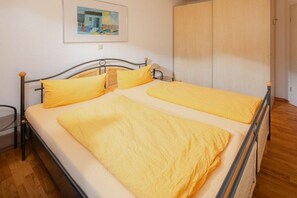A single bed with a metal frame and yellow bedding, a wooden floor, and a door to the right. - Holiday apartment in Juist with swimming pool (Juist)