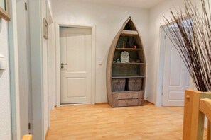 A hallway with wooden flooring, a white door, and a wooden shelf unit with baskets. - Holiday home with 3 bedrooms (born an der darss)