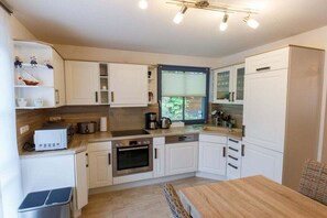 A modern kitchen with white cabinetry, a built-in oven, a coffee maker, and a window with blinds. - Holiday home with 3 bedrooms (born an der darss)