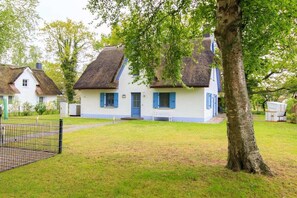 Et traditionelt hus med stråtækt tag, dør i blå farve og hvide vægge.