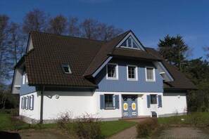 Ein zweistöckiges Haus mit geneigtem Dach, einer Veranda und einem kleinen Garten.