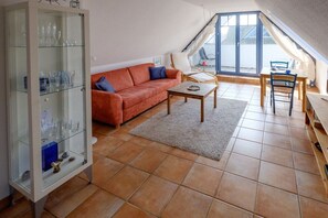 Ein Wohnzimmer mit einer Couch, einem Couchtisch, einer Vitrine und Blick durch ein großes Fenster.