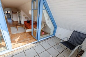 A room with a glass door leading to an outdoor area, a sofa, a chair, and a small table. - Sonnenhof Top Floor D5 (Prerow)