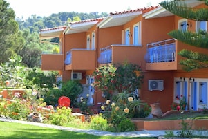 Un edificio de varios pisos con balcones, unidades de aire acondicionado y un jardín con diversas plantas y flores.