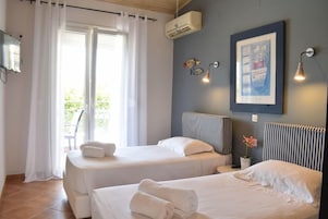 Habitación de hotel con dos camas, un ventanal con cortinas, un equipo de aire acondicionado, un televisor montado en la pared y un cuadro enmarcado.