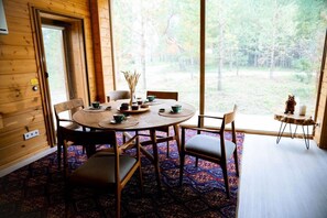 A wooden interior with a round table set for dining, chairs, and a view of a forest through large windows. - Wyndham Residences Aqkol (Astana)