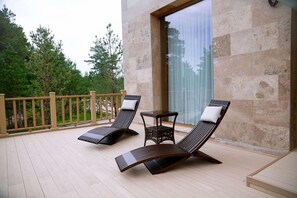A balcony with two lounge chairs and a small table, overlooking a garden with trees. - Wyndham Residences Aqkol (Astana)