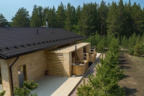 Una cabana de fusta amb un teulat inclinat, una terrassa de fusta i una sauna.