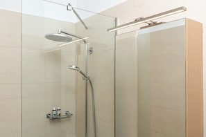 A modern shower with a handheld showerhead and a wall-mounted rain showerhead, a glass enclosure, and a light fixture above. - Venti Di Paxos 2 | One -Bedroom Apartment, Apartment (Paxoi)
