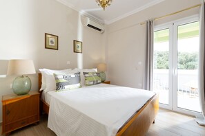 A hotel room with a bed, bedside tables, a lamp, and a view of the outdoors. - Venti Di Paxos 2 | One -Bedroom Apartment, Apartment (Paxoi)