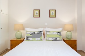 A bed with two pillows, two bedside lamps, and two framed pictures on the wall. - Venti Di Paxos 2 | One -Bedroom Apartment, Apartment (Paxoi)