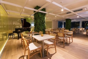 A restaurant with a piano, tables, chairs, and a large vertical garden. - Janga Boutique Hotel (Maragogi)