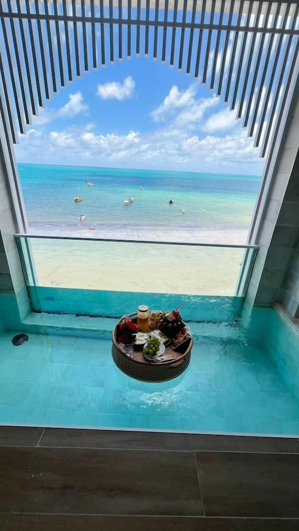Blick aus einem Fenster auf eine Strandansicht, ein Pool mit einem schwimmenden Tablett und einen klaren Himmel.