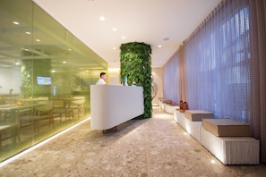 A reception area with a white reception desk, a green vertical garden, and a seating area with cushioned benches. - Janga Boutique Hotel (Maragogi)