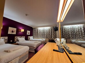 Habitación de hotel con dos camas, una mesa de madera, un televisor y una ventana con cortinas.