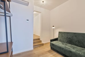 Ein modernes Wohnzimmer mit einem grünen Sofa, Holzboden, einer Treppe und einer Lampe.