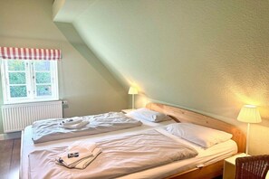 A single bed with a wooden headboard, a window with a checkered valance, and a bedside lamp. - Old Registry Office Large Apartment (Oldsum)