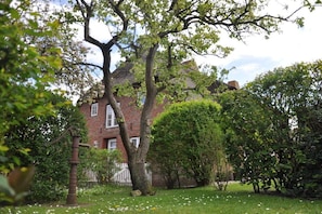 A traditional brick house with a white fence, surrounded by lush greenery and a well-maintained lawn. - Old Registry Office Large Apartment (Oldsum)