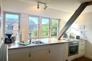 A kitchen with a large window, a dishwasher, an oven, and a coffee maker. - Old Registry Office Large Apartment (Oldsum)