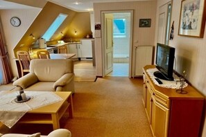 Un salon chaleureux avec un canapé, un téléviseur posé sur un meuble en bois et un coin repas comprenant une table et des chaises.
