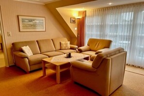 A living room with a sofa set, a coffee table, and a window with curtains. - Hansen Grevelingstieg 16 (Nieblum)