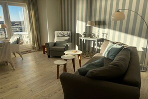 A living room with a sofa, armchair, and small round tables. - Holiday apartment in Wyk on Föhr with balcony (Wyk auf Föhr)