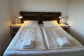 Ein Doppelbett mit weißen Bettwäsche und zwei Nachttische, jeweils mit einer Lampe.