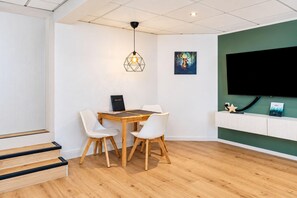 A modern room with a wooden dining table, white chairs, a hanging light fixture, a mounted TV, and a framed artwork on the wall. - Modern apartment in the heart of Römhild, Thuringia (Römhild)