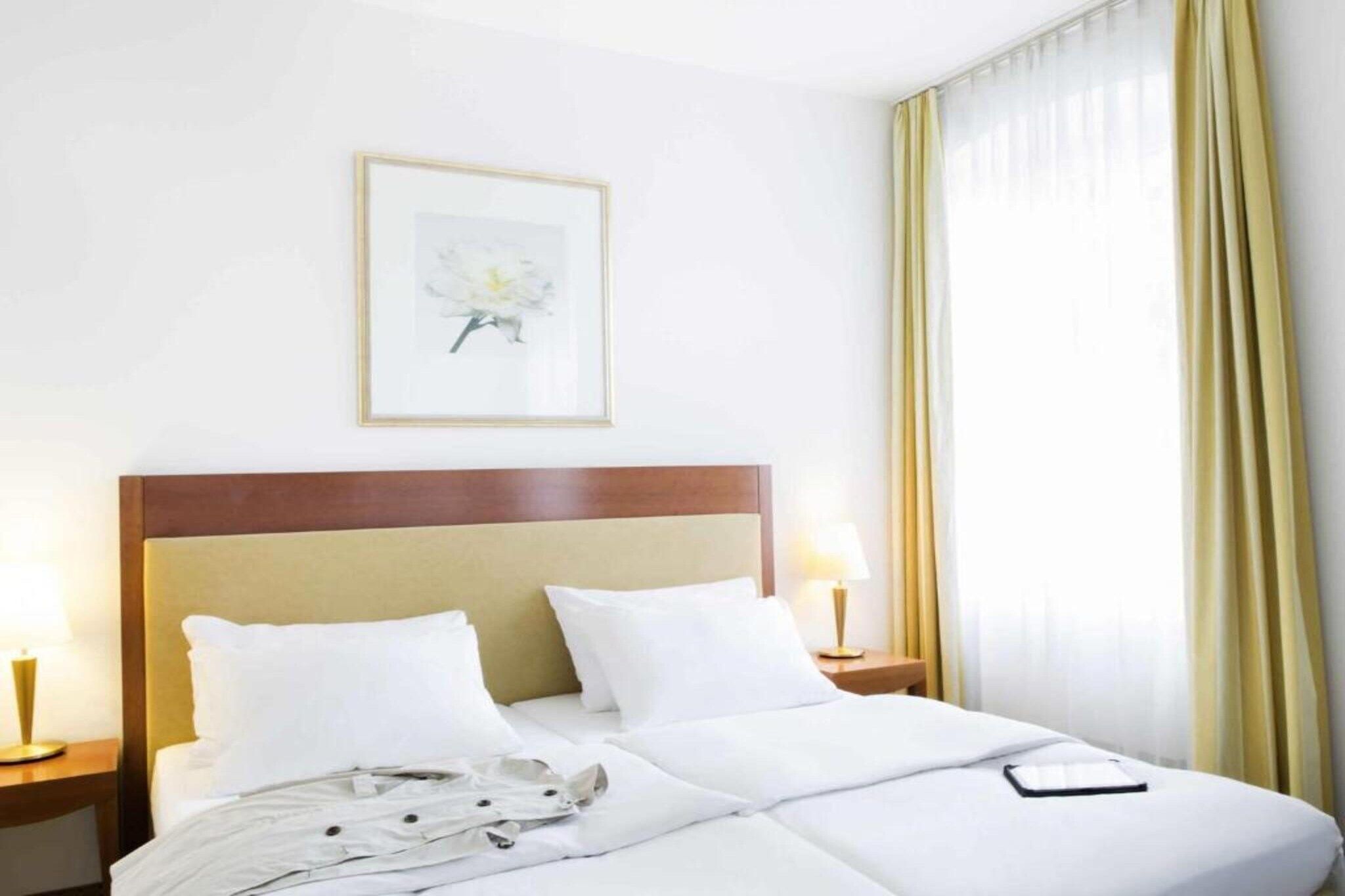 Una camera d'albergo con un letto, un quadro appeso al muro e una finestra con tende.